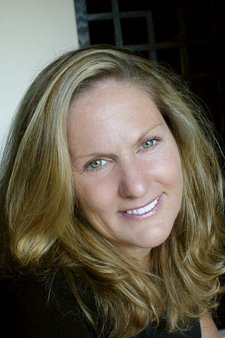 A woman with long brown hair is smiling and posing for the camera, wearing a black top.