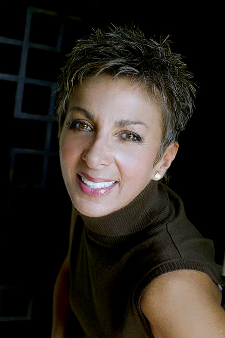 A woman with short hair and a brown top, smiling at the camera.