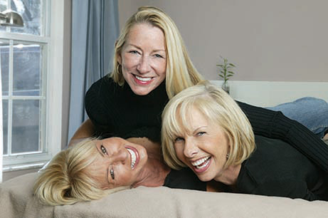 Three women lying on a bed, smiling and posing for the photo.