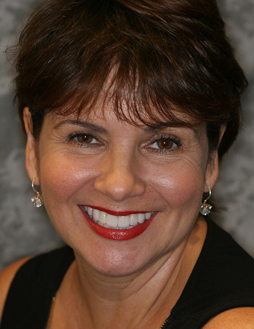 Woman with short hair, wearing a black top and earrings, smiling at the camera.