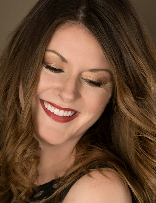 The image features a woman with long hair, wearing makeup and a black top, smiling at the camera.