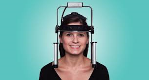 The image is a photograph of a person wearing a virtual reality headset, with the individual s face visible, and the background is plain and light-colored.