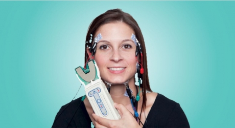 A woman holding a device with electrodes on her head.