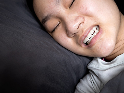 The image shows a young person with their eyes closed, lying in bed with a pillow and a dark background.