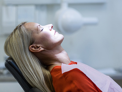 A woman with blonde hair is seated in a dental chair, wearing a protective face mask and appears to be undergoing a dental procedure or examination.