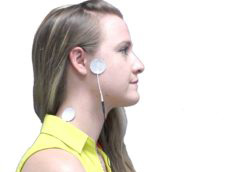 A person in a yellow top wearing a device with electrodes on their neck and shoulders.