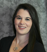 A young woman with long hair smiling at the camera, wearing a black top and a necklace.