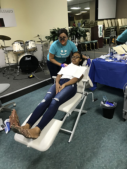 A person sitting in a dental chair, receiving dental care from a professional.