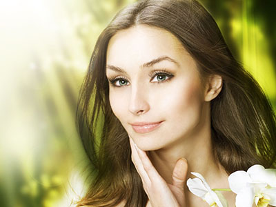 A woman with fair skin and long hair, wearing makeup, set against a blurred background of natural elements.