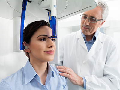 The image shows a woman sitting in a dental chair with a blue mouthpiece, receiving dental care from a dentist who is standing to her right.