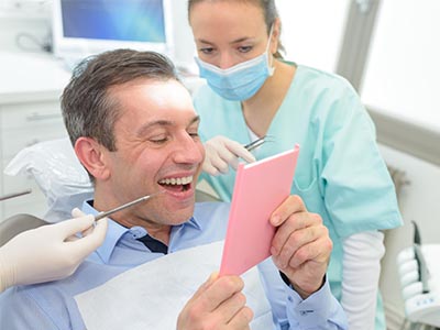 The image shows a man holding a pink card in front of his face, surrounded by dental professionals in a dental office setting.