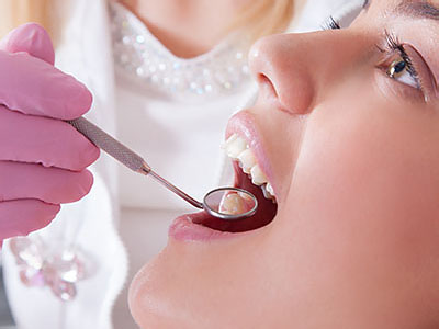 A dental professional is performing a procedure on a patient s teeth, with the patient wearing a pink surgical mask and having their mouth open.