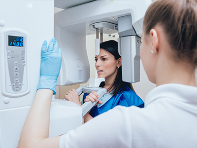 Two individuals in a medical or dental setting, with one person operating a large, modern imaging machine and the other observing.