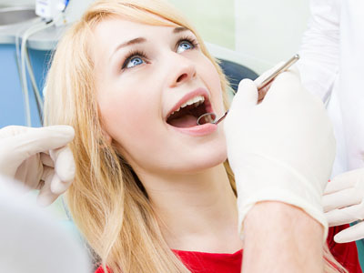 A woman in a dental chair receiving dental care, with a dentist performing the procedure and assistants present.