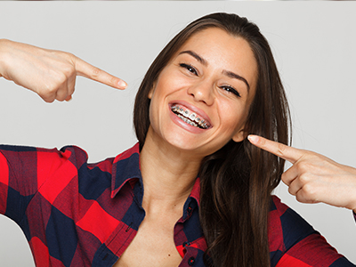 A woman with a toothy smile pointing at her teeth, showcasing dental implants.