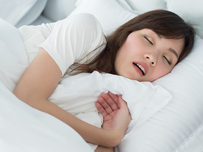 A person is sleeping in a bed with white sheets and pillow, their eyes are closed and they appear relaxed.