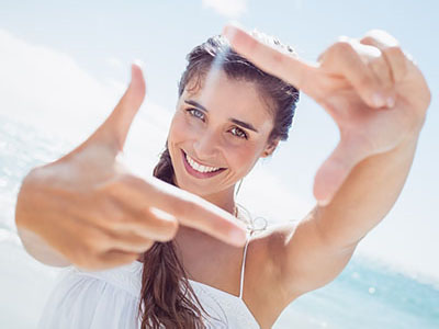 A woman taking a selfie with her hand in front of her face, smiling and posing for the camera.