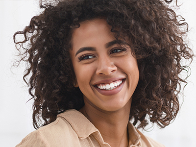 A smiling woman with curly hair and a warm smile, wearing a brown top.